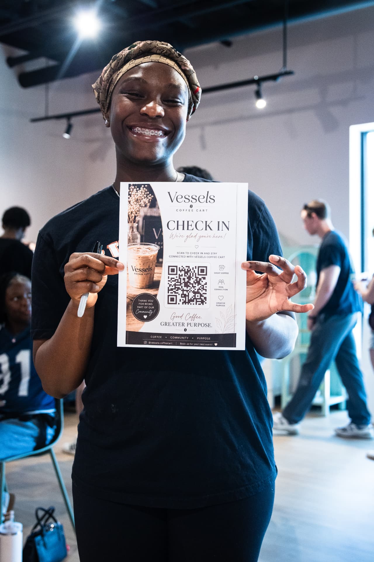 Team member holding a Vessels Coffee check-in sign at an event